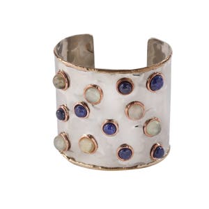 May include: A silver cuff bracelet with a hammered finish and a copper trim. The bracelet is decorated with a variety of blue and white gemstones.