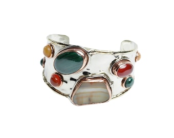 May include: A silver cuff bracelet with a hammered finish and colorful stones. The stones are green, red, orange, and white.