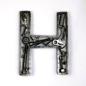 May include: A metal letter H made of a chain link frame filled with various metal parts, including bolts, nuts, and a spark plug.