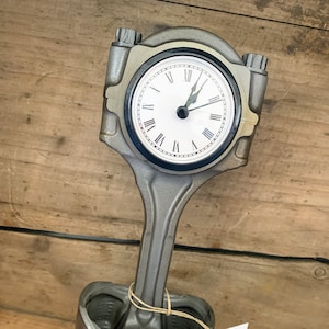 Clock made out of a car engine's piston finished in gunmetal gray with a black clock ring.