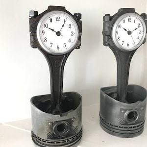 Two car piston clocks - left clock has a patina finish with a silver clock ring, and right clock has an elegant finish with a silver clock ring.