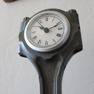 Close-up view of a clock made out of a car engine's piston finished in gunmetal gray with a silver clock ring.