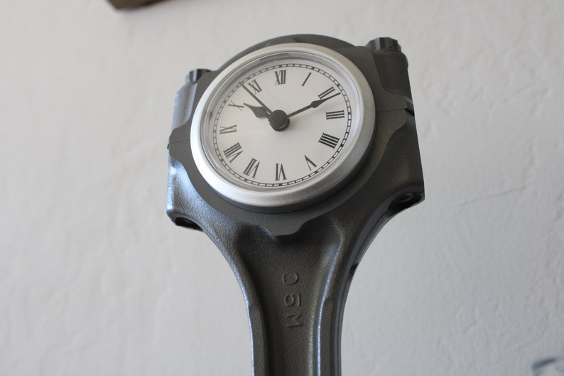 Close-up view of a clock made out of a car engine's piston finished in gunmetal gray with a silver clock ring.