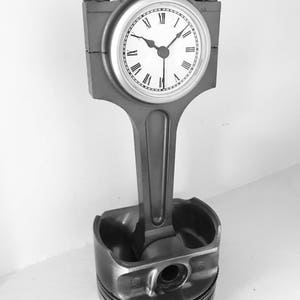 Clock made out of a car engine's piston finished in gunmetal gray with a silver clock ring.