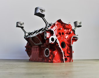 May include: A red engine block with four pistons and connecting rods. The engine block is disassembled and the pistons are in the up position.