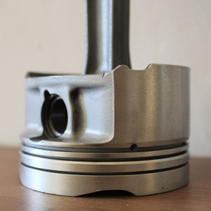 Close-up view of the base of a clock made out of a car engine's piston, finished in gunmetal gray.