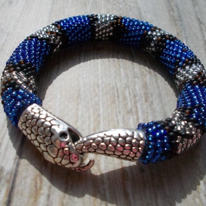 Könnte beinhalten: Ein blaues, schwarzes und silbernes Perlenarmband mit einem Schlangenkopfverschluss.
