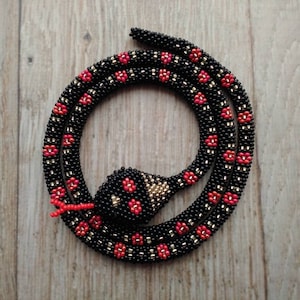 May include: A black beaded snake necklace with red and gold accents. The snake is coiled and has a beaded head.