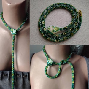 Può includere: Una collana di perline verdi e dorate con un ciondolo a forma di testa di serpente. La collana è realizzata con piccole perline e ha un design lungo e fluido.