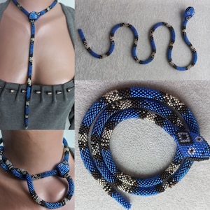 May include: A beaded snake necklace with a blue, black, and silver color scheme. The snake is coiled into a circle and has a head with black eyes. The necklace is approximately 40 inches long.