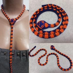 Può includere: Una collana di serpente con perline con un motivo blu e arancione. La collana è mostrata in due stili diversi, uno come un ciondolo lungo e l'altro come un serpente avvolto.