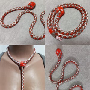 Può includere: Una collana di serpente con perline in un motivo rosso, bianco e marrone. Il serpente è avvolto e ha una testa di perline con occhi rossi.