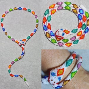 Può includere: Un set di collana e bracciale a forma di serpente con perline. I gioielli presentano una base bianca con perline colorate a forma di foglia in vari colori. La testa del serpente è bianca con dettagli rossi e blu.