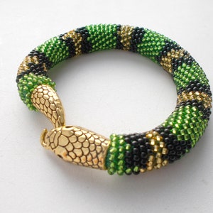 Könnte beinhalten: Ein grünes, schwarzes und goldenes Perlenarmband mit einem goldenen Schlangenkopfverschluss.