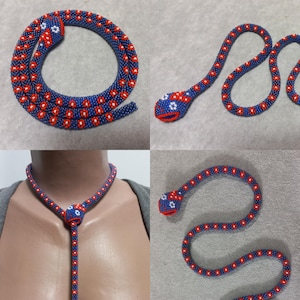 May include: A beaded snake necklace with a blue and red patterned design. The necklace is made of small beads and has a snake head at the end. The snake head is also beaded and has a white and red flower design.