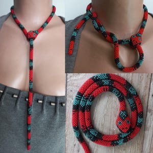 May include: A red and black beaded snake necklace with a turquoise accent. The necklace is made of small beads and is shaped like a snake with a head at one end. The snake is coiled up and the head is facing the camera.