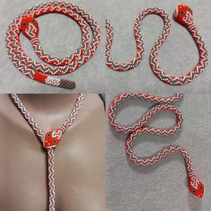 Può includere: Una collana di serpente con perline con un motivo rosso, bianco e marrone. Il serpente è avvolto e ha una testa di perline.