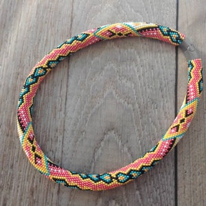 May include: A colorful beaded necklace with a geometric pattern in shades of pink, yellow, turquoise, white, and black. The necklace is made of small beads and has a silver clasp.