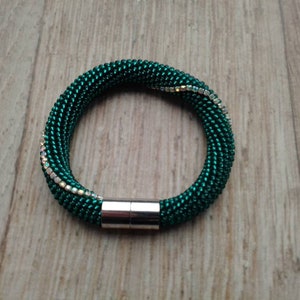 Pode incluir: Um bracelete de contas verdes com fecho magnético e uma fila de contas iridescentes.