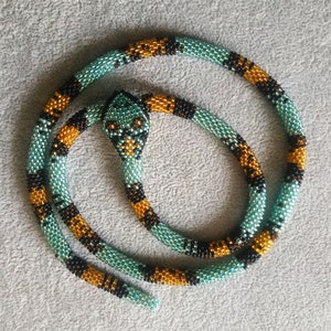 Op de afbeelding: Een kralen slangenketting in turquoise en goudkleurige tinten. De slang is opgerold en heeft een kralenkop.
