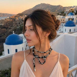 May include: A long, flexible beaded necklace featuring a black and white snake-like pattern. The necklace is wrapped around the neck and hangs down in a loop, with a detailed head and tail design at the ends, crafted from small, uniform beads.