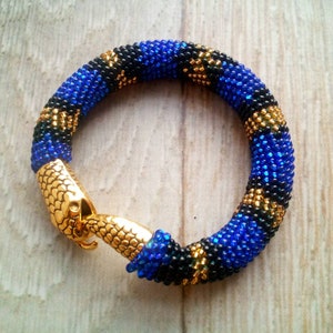 May include: A beaded bracelet with a snake-shaped clasp. The bracelet is made with blue, black, and gold beads.