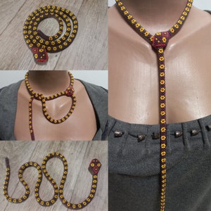 May include: A beaded necklace in the shape of a snake with a brown and yellow pattern. The necklace is shown on a model and laid flat on a wooden surface.