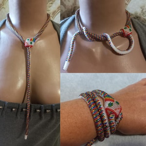 Op de afbeelding: Een kleurrijke kralenketting in de vorm van een slang. De ketting is lang en heeft een kralenkop met een regenboogpatroon. De ketting wordt om de nek gedragen en als armband.