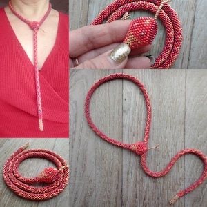 May include: A red and gold beaded snake necklace. The necklace is made of small beads and is shaped like a snake. The snake's head is raised and has a gold bead for an eye.