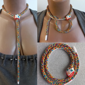 Op de afbeelding: Een kleurrijke kralen slangenketting met een witte kop en rode ogen. De ketting kan worden gedragen als een choker of een lange hanger.