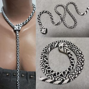 Può includere: Una collana di serpente in perle nere e bianche. Il serpente è avvolto e presenta un motivo geometrico. La collana è abbastanza lunga da essere indossata come un choker o un laccio.