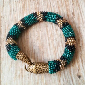 Könnte beinhalten: Ein grünes, schwarzes und goldenes Perlenarmband mit einem Schlangenkopfverschluss aus Bronze.