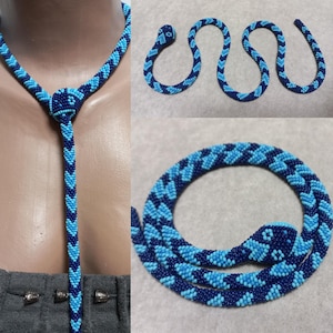 Può includere: Una collana di serpente in perle blu e turchese. Il serpente è fatto di piccole perle e ha un motivo a chevron. La collana è abbastanza lunga da essere indossata come un choker o un ciondolo.