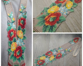 May include: A long beaded necklace with a floral design featuring red, yellow, and green beads. The necklace is made of small beads and has a fringe at the bottom.