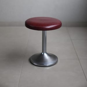 May include: A red vinyl padded stool with a silver metal base.