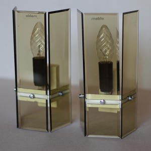 May include: Pair of brown glass wall sconces with clear light bulbs. The sconces have a white label with the text "olden" and "meblo" on them.
