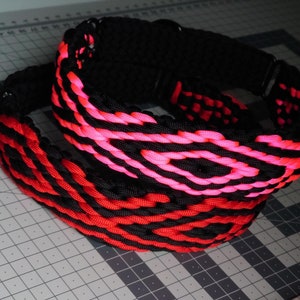 Puede incluir: Un collar de paracord enrollado que presenta un patrón de diamantes repetitivo tejido en cuerda de color rosa neón vibrante y negro sólido. El diseño incluye una hebilla y herrajes de metal negro, con un tejido grueso y texturizado.
