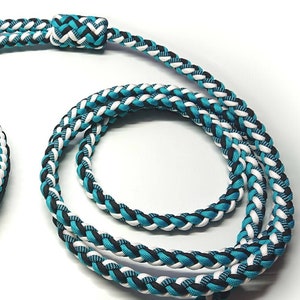 Puede incluir: Un conjunto de collar y correa trenzados para mascotas con un patrón tejido en turquesa, negro y blanco. El collar incluye una hebilla de plástico negro y una anilla en D, mientras que la correa cuenta con un mosquetón giratorio de metal plateado.