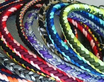 May include: A collection of braided paracord collars in various color combinations including red, pink, blue, purple, green, yellow, black, and grey. Each collar features a circular metal ring attachment for secure fastening and durable construction.