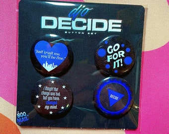 May include: A set of four black and blue button pins with different sayings. The pins are packaged on a black card with the words "dio DECIDE BUTTON SET" printed on it. The sayings on the pins are "just trust me, you'll be fine", "GO FOR IT", "I thought that change was bad but you have changed my mind", and "DECIDE".