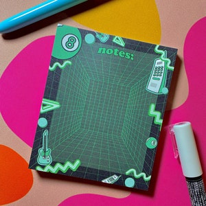 May include: A green and black notepad with a grid pattern and retro-themed graphics, including a video game controller, a phone, a guitar, and a pool ball. The notepad has the number "8" and the word "notes:" printed on it.