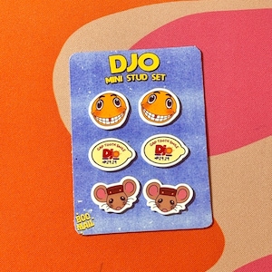 Könnte beinhalten: Eine blaue Karte mit einem "DJO MINI STUD SET" mit sechs Mini-Ohrsteckern. Die Ohrringe zeigen lächelnde Gesichter, Lächeln mit Zahnlücken und Maus-Designs. Die Karte liegt auf einem bunten orange-rosa gemusterten Hintergrund.