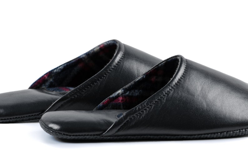 May include: Two pairs of black leather slippers with a plaid lining. The slippers have a closed toe and a slip-on design.
