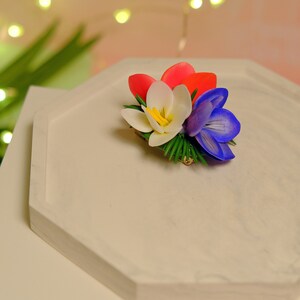 May include: A white, red, and blue flower arrangement with green leaves. The flowers are made of fabric and are arranged in a cluster.