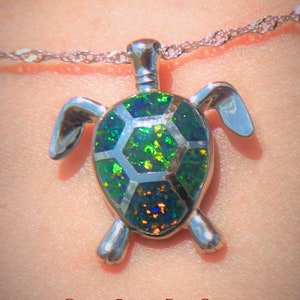 May include: A silver turtle pendant with a green, black, and gold fire opal inlay. The pendant is on a silver chain and the text "GREEN BLACK FIRE OPAL PLATINUM ON SILVER" is below the pendant.