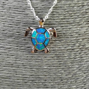 May include: A silver chain necklace with a blue opal turtle pendant. The turtle is detailed with a textured shell and has a silver body.