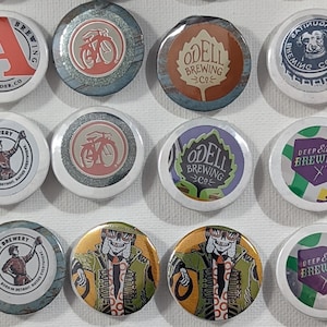 May include: Collection of round pinback buttons featuring brewery logos and designs. Includes logos for Avery Brewing, Odell Brewing, Deep Ellum Brewing Co., and Atwater Brewery. Some buttons have a bicycle graphic or a skeleton illustration.