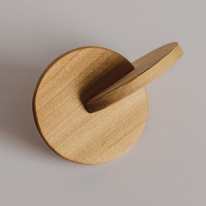 May include: A wooden toy with a round base and a smaller, curved piece attached to the side. The toy is made of light brown wood and has a smooth, polished finish.