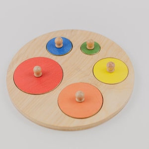 May include: A wooden circle puzzle with five colorful circles that fit into the corresponding holes. The circles are red, orange, yellow, green, and blue.