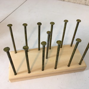 May include: A wooden board with 13 rusty nails hammered into it. The nails are arranged in a staggered pattern.